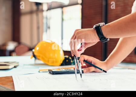 Architect using divider compass working on blueprint. blueprints, ruler, calculator, safety hat and book on the table. Construction concept. Engineeri Stock Photo