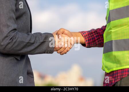 Businesswomen and foreman shake hands together. Engineer and manager teamwork and checking at site construction . Stock Photo