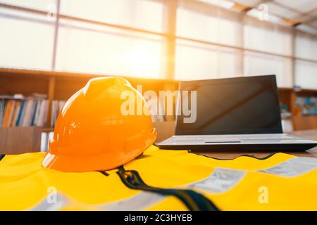 Safety work at Industrial and Factory concept. Engineer Construction Safety hat helmet on office working desk with laptop. Stock Photo
