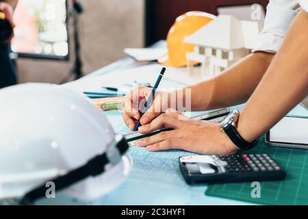engineers holding a pen pointing to a building and  drawing outlay construction plan as guide for builders with details Stock Photo