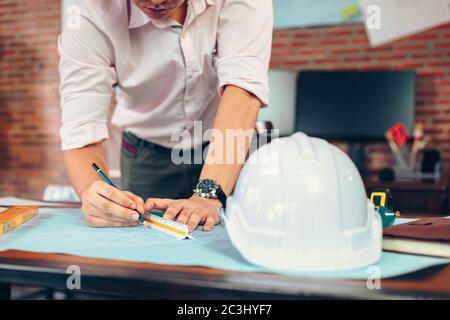 engineers holding a pen pointing to a building and  drawing outlay construction plan as guide for builders with details Stock Photo