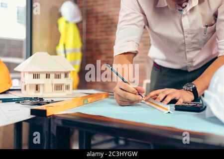 engineers holding a pen pointing to a building and  drawing outlay construction plan as guide for builders with details Stock Photo
