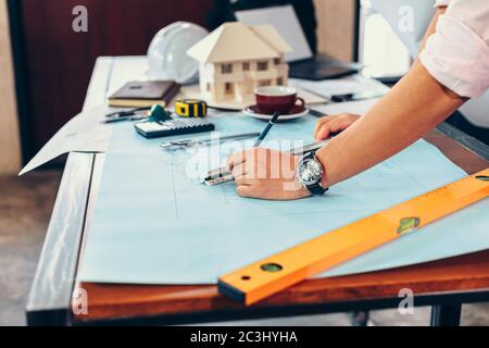 engineers holding a pen pointing to a building and  drawing outlay construction plan as guide for builders with details Stock Photo