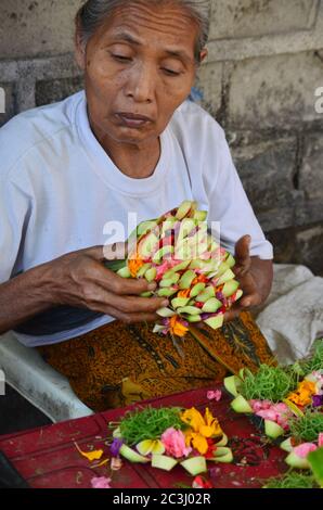 Balinese woman making the offering flower with fresh tropical flowers. Canang Sari is a symbol of gratitude for Balinese Hinduism. Stock Photo