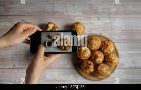 Woman taking a photo of coffee and muffins with a smartphone. Homemade food photo for social media. Stock Photo