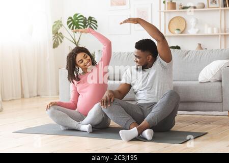 Active african expecting couple exercising together at home Stock Photo