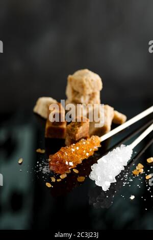 Homemade sugar candies or crystallized sticks and heap brown cane cubes sugar on a black background with reflection, copy space. Stock Photo