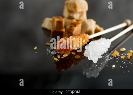 Homemade sugar candies or crystallized sticks and heap brown cane cubes sugar on a black background with reflection, copy space. Stock Photo