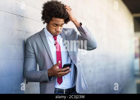 Worried Black Businessman using his smartphone outdoors. Stock Photo