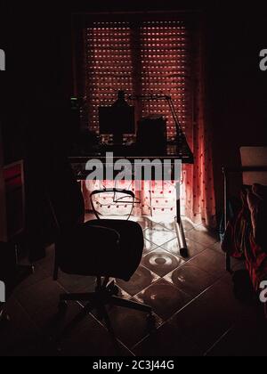 Vertical high angle shot of a dark workplace near a panoramic window closed with red curtains Stock Photo