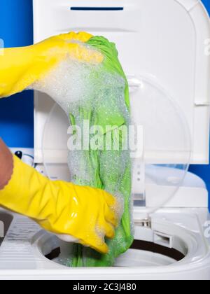 a person with yellow gloves taking green clothes out of a washing machine with foam Stock Photo