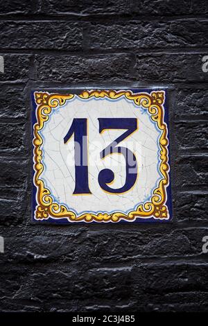 Decorative delftware tile with the number 13, on a black painted wall in Amsterdam, Stock Photo