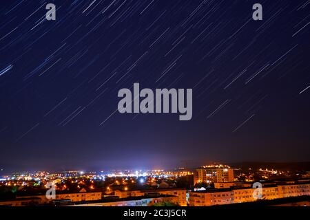 Star Trails in clear night sky above city Stock Photo