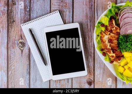 Tablet and notebook with healty nutrition salad on wooden table. Stock Photo