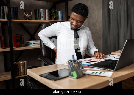 Successful young african businessman tired to sit at his desk in the office, working on laptop  Stock Photo