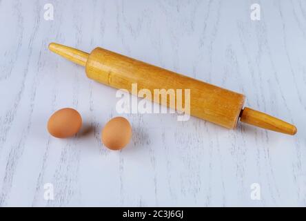 Rolling pin and two brown eggs on white table. Stock Photo