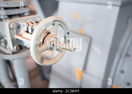 Industrial blue painted pipeline flanges, hand wheel and valve closeup, out of focus industrial machinery background. Old rusty control equipment Stock Photo