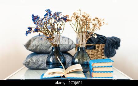 Cozy home interior decor: stack of books, vase with flowers, pillows and plaid on a white table. Distance home education. Quarantine concept of stay h Stock Photo