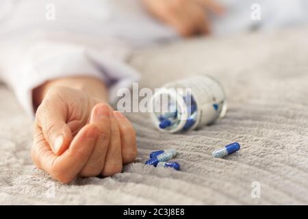 Woman’s hand close up committing suicide by overdosing on medication, pills and bottle beside. Overdose pills and addict concept background Stock Photo