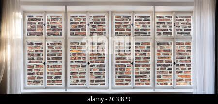 No view, loneliness, brick wall fence background through old window concept. Vintage white window pane with frame, handles and sill. Sunbeams on curta Stock Photo