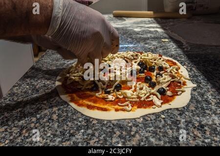 Preparation of the Italian pizza. Pizza four Seasons. Sauce, mushrooms, black olives, artichokes, mozzarella Stock Photo