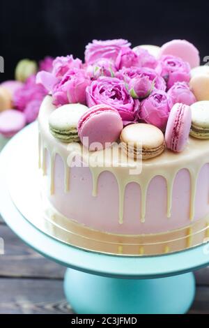 Elegant pink wedding cake decorated with melted white chocolate, beautiful fresh roses and french macaroons. Black background. Stock Photo