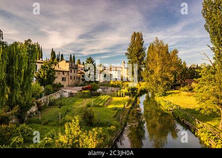 The Chiasco river that crosses the ancient medieval village of Bevagna. Perugia, Umbria, Italy. Trees, vegetation, cultivated gardens. The blue sky at Stock Photo