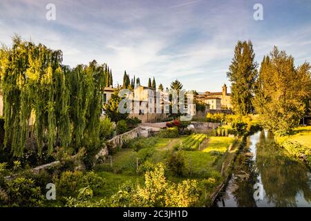 The Chiasco river that crosses the ancient medieval village of Bevagna. Perugia, Umbria, Italy. Trees, vegetation, cultivated gardens. The blue sky at Stock Photo