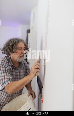 Worker man with curly hair plastering an inside wall covering orange corrugated electrical tube. Stock Photo