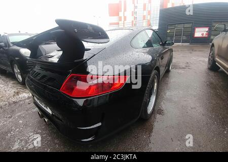 Moscow, Russia - April 22, 2019: A black Porsche 911 customized with aerodynamic kit and carbon spoiler stands in the parking lot at the service center. Rain drops on the car. back side view Stock Photo