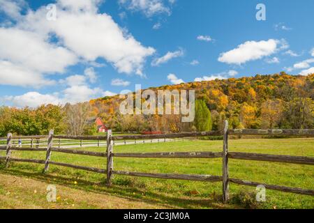 From American country road a rural landscape with red barn in distance beyond rustic post and rail fence in Kent county, New England USA.