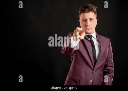 Law student with blond hair dressed in burgundy jacket, white shirt and black tie doing I am watching you gesture posing on isolated black background Stock Photo