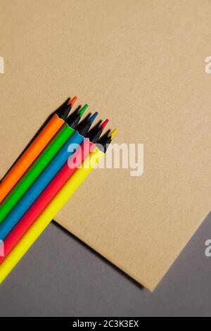five colored pencils lie on  kraft notebook gray background, top view Stock Photo