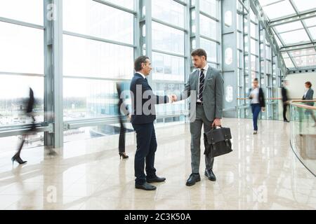 Business people shaking hands standing in a crowd of walking people Stock Photo