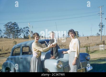 Castle Hill, Sydney Australia Winter 1958: Two young Australian women, one with a young boy standing on the bonnet (hood) of an FX 48-215 Holden car stand Stock Photo