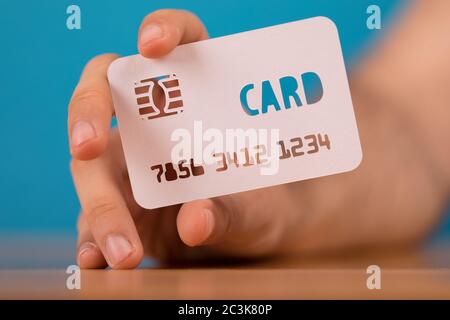 Closeup shot of a person holding a credit card paper cut-out on a blue blurry background Stock Photo