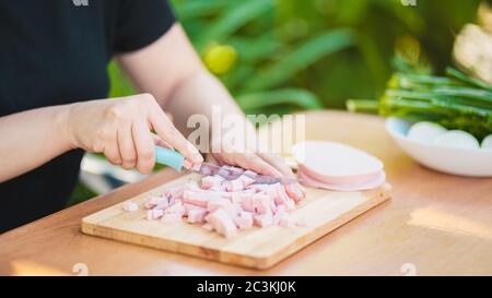 Young woman cutting sausage on wooden board outdoors. Women's hands cutting sausage goods with knife on chopping board. Stock Photo