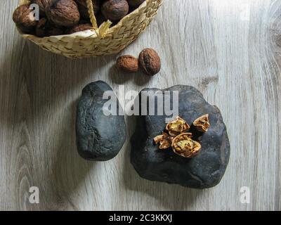 Fresh organic walnuts are  into a wicker basket next to Walnuts broken on the stone on wooden table. Whole Ripe walnut kernels. Close up. Top view. He Stock Photo