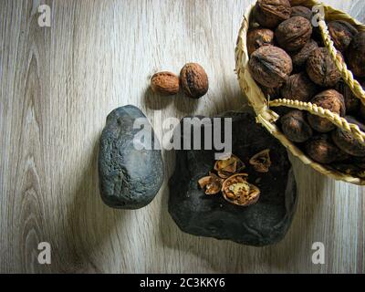 Organic Ripe walnuts are  into a wicker basket next to Walnuts broken on the stone on wooden table. Close up. Top view. Healthy lifestyle. Stock Photo