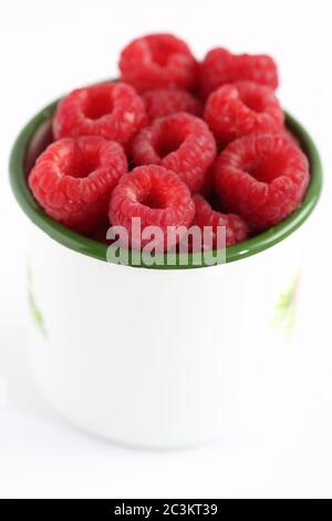 White mug cup filled with fesr eco raspberries close up isolated on white background. Stock Photo