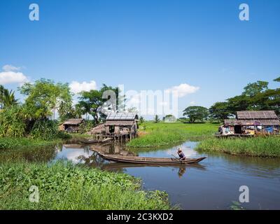 MAUBIN, MYANMAR - NOVEMBER 12, 2014: Man paddling past farmers' houses in Maubin, Ayeyarwady Division in Southwest Myanmar. Many homes in the area lac Stock Photo