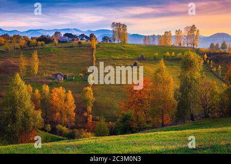 Wonderful autumn rural scenery and colorful deciduous trees on the slopes. Houses and gardens on the hill at sunset, Carpathians, Transylvania, Romani Stock Photo