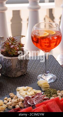 Aperol spritz in big glass red summer cocktail, cheease, meat, nuts snacks served on black board, terrace party. High quality photo Stock Photo