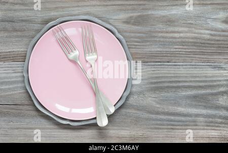 Two vintage forks on an empty pink plate on an old gray wooden background with copy-space Stock Photo
