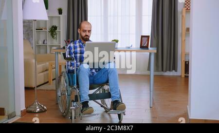 Handicapped freelancer in wheelchair working on laptop. Stock Photo