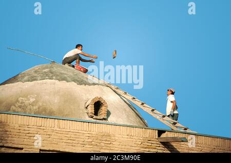 Two uzbek male builders, restoring and repairing old roof and throwing bricks to each other at Shah-i-Zinda, in Samarkand, Uzbekistan Stock Photo