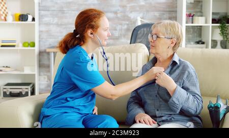 Caucasian female doctor in nursing home listening old woman heartbeat with stethoscope Stock Photo