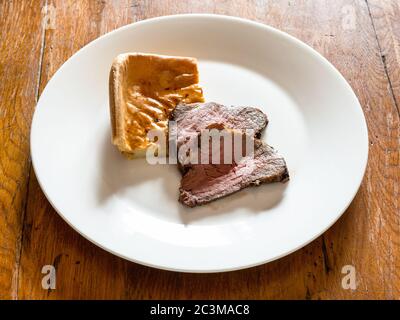 home-made sliced Roast Beef and piece of Yorkshire pudding on white plate on old wooden table at home kitchen Stock Photo