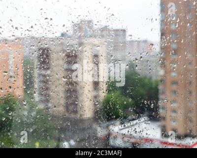 raindrops on window glass and view of blurred apartment houses on background in rain in summer (focus on drops on surface of windowpane) Stock Photo