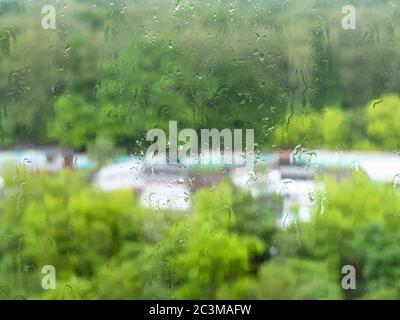raindrops on window glass and view of blurred green city park in rain on background in summer (focus on drops on surface of windowpane) Stock Photo